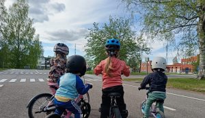 Kuvassa neljä pientä lasta on kuvassa potkupyörien kanssa selkä kameraan päin.