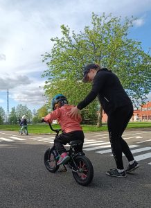 Kuvassa aikuinen auttaa lasta oppimaan polkupyöräilyä.